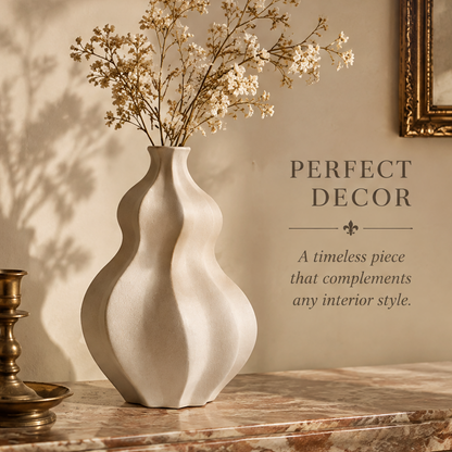 Cream wave-shaped vase with dried flowering stems displayed on a marble console beside a candleholder